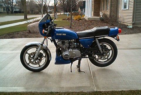 1985 Ford Crown Victoria LTD - A blue Suzuki motorcycle is parked on a concrete driveway in front of a house.
