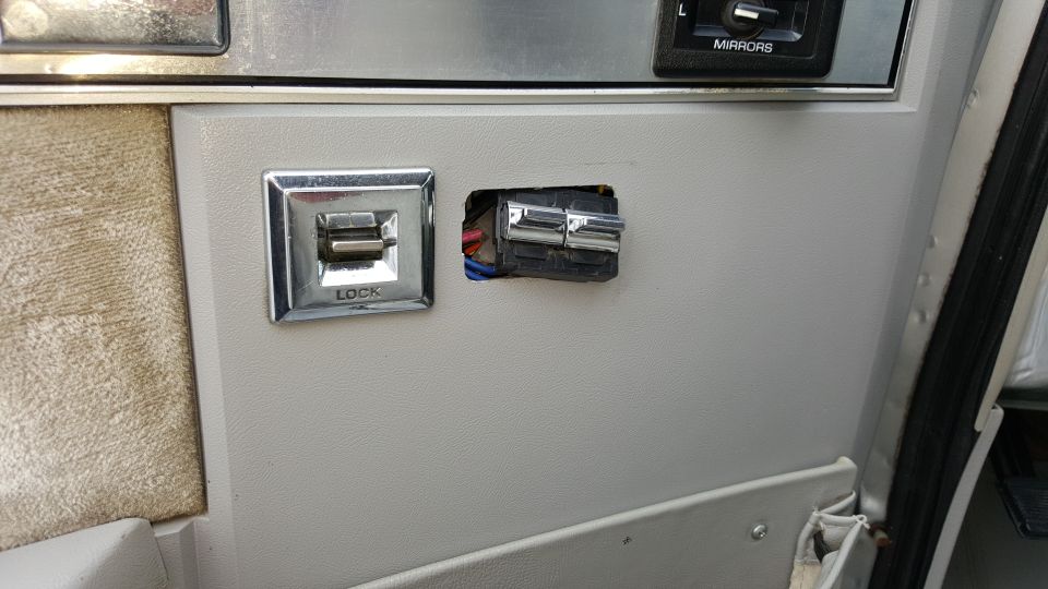 Interior door panel showing a power window lock switch and an empty slot for another switch. The word 'LOCK' is visible on the switch