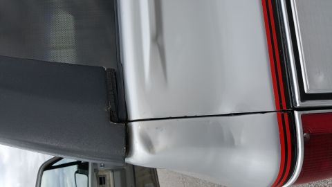 1995 Ford Bronco - Close-up of damage to the rear quarter panel and trim of a silver vehicle.