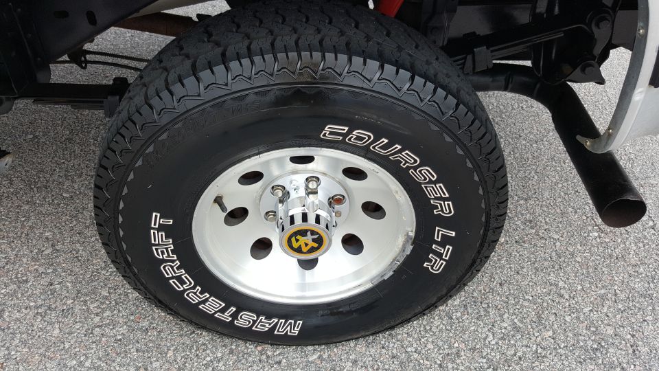 Silver alloy wheel with Mastercraft Courser LTR tire, chrome lug nuts, and yellow emblem on hub