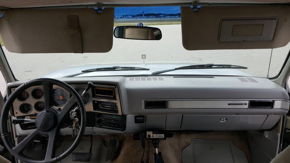 Dashboard and steering wheel of an older truck, looking out the windshield at an open area