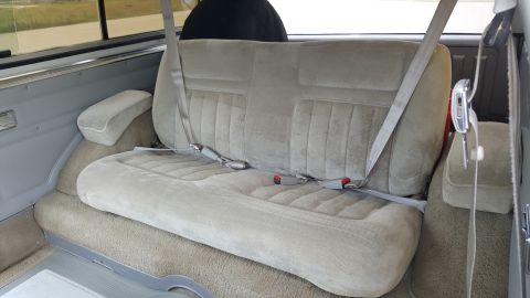 1995 Ford Bronco - The interior of a vehicle shows a fabric bench seat with seatbelts.