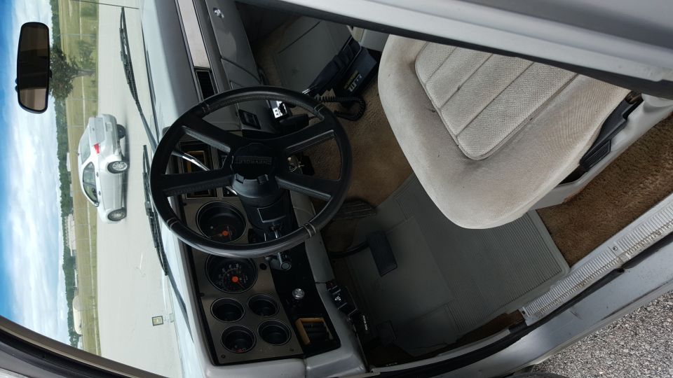 Interior view of an older pickup truck, showing the dashboard, steering wheel, and passenger seat. A silver car is visible through the windshield