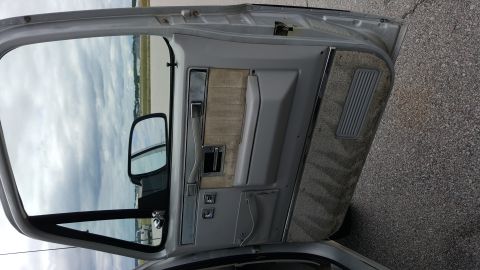 1995 Ford Bronco - Interior view of a vehicle's gray door panel, showing fabric inserts and controls. The side mirror is visible through the open door.