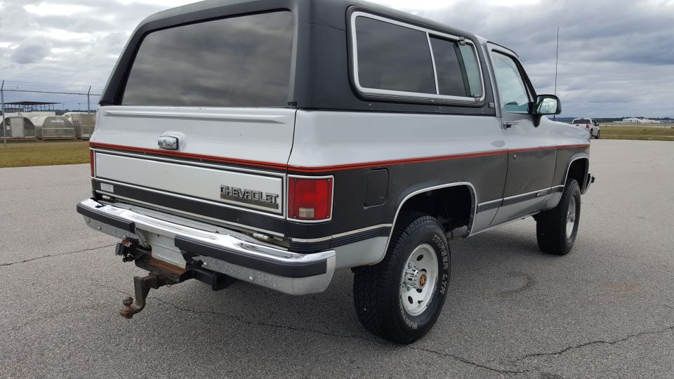 Rear view of a two-tone silver and dark gray Chevrolet K5 Blazer with a black top and tow hitch
