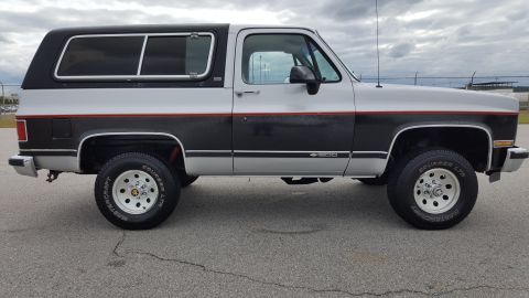 1995 Ford Bronco - This two-tone SUV features a black camper shell and a distinctive red-lined stripe along its side.