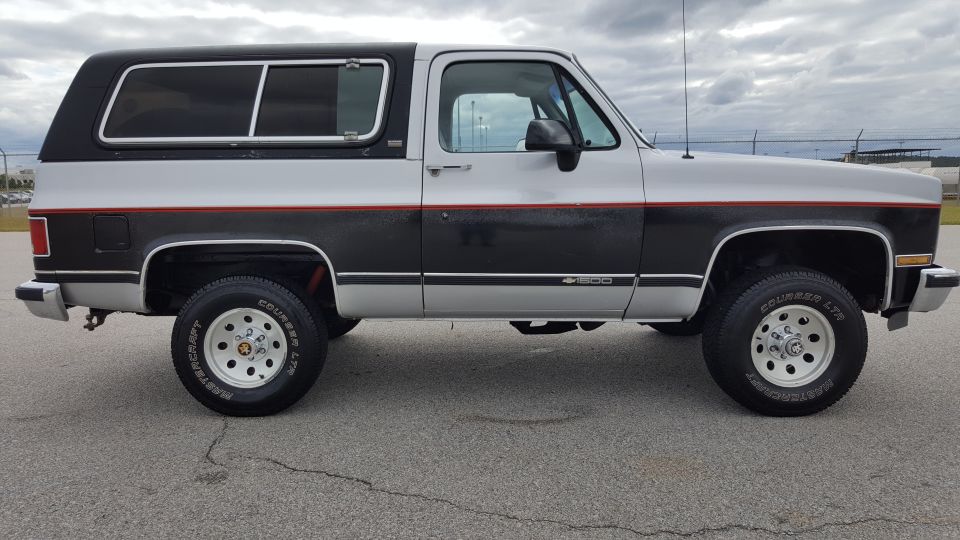 Side view of a two-tone SUV with a black camper shell. It has a black stripe with a red pinstripe separating the silver and black paint