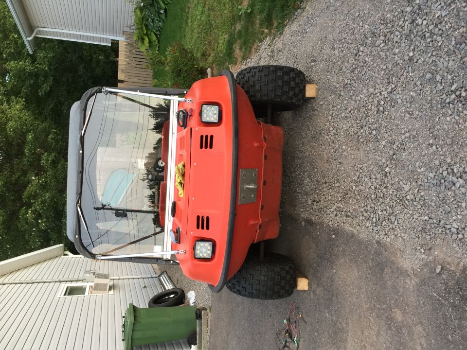 Orange amphibious ATV with a black canopy, parked on gravel. It has four large tires and square headlights