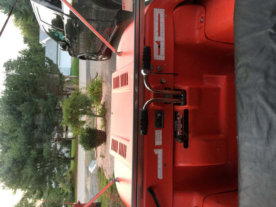 Red vehicle interior with two levers and a black fabric cover. A black SUV is visible outside