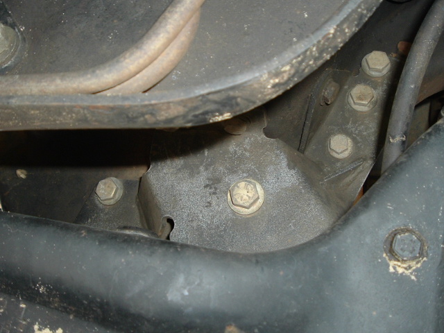 Close-up of black metal bracket with hex bolts and rust, covered in dust and grime.
