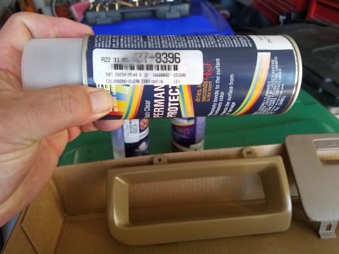 1994 Ford Bronco - A hand holds a spray can of clear coat above tan plastic car interior trim pieces.