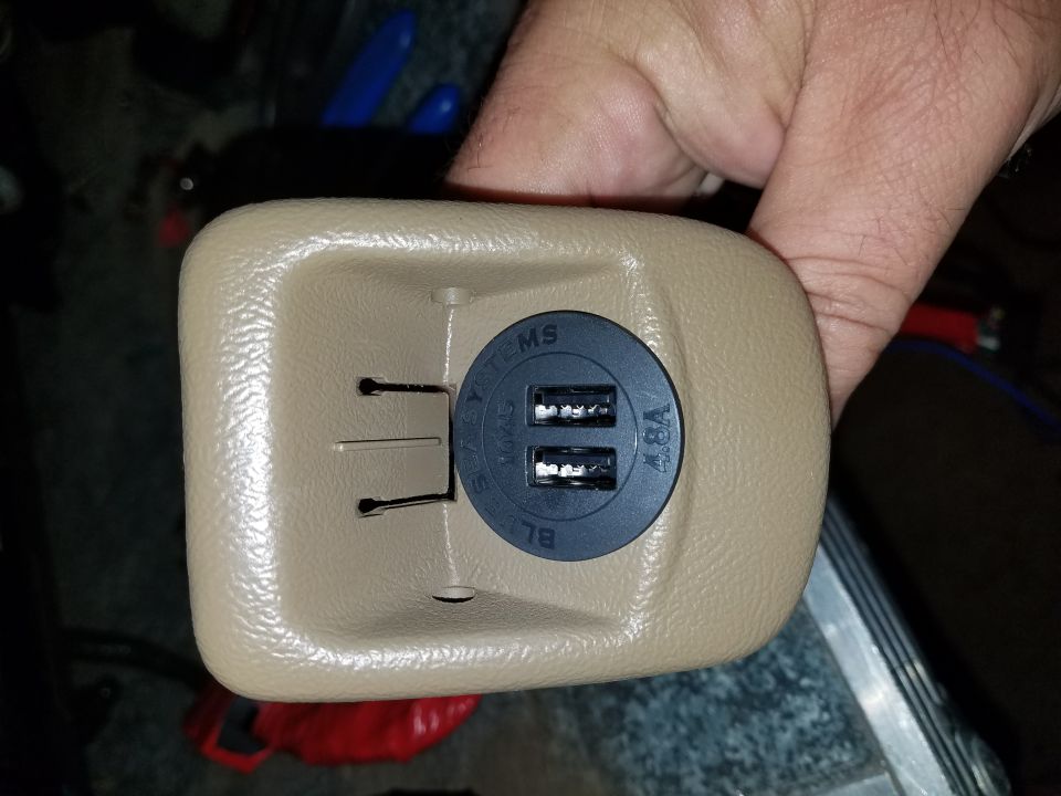 Close-up of a tan plastic housing with a black circular insert containing two USB ports and "4.8A" text. Some wires are visible