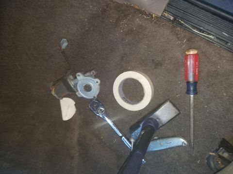 1994 Ford Bronco - Tools and a disassembled window motor are laid out on the carpeted floor of a vehicle.