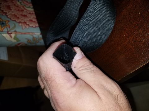 1994 Ford Bronco - Close-up of black seatbelt webbing being manipulated by a hand, with furniture in the background.