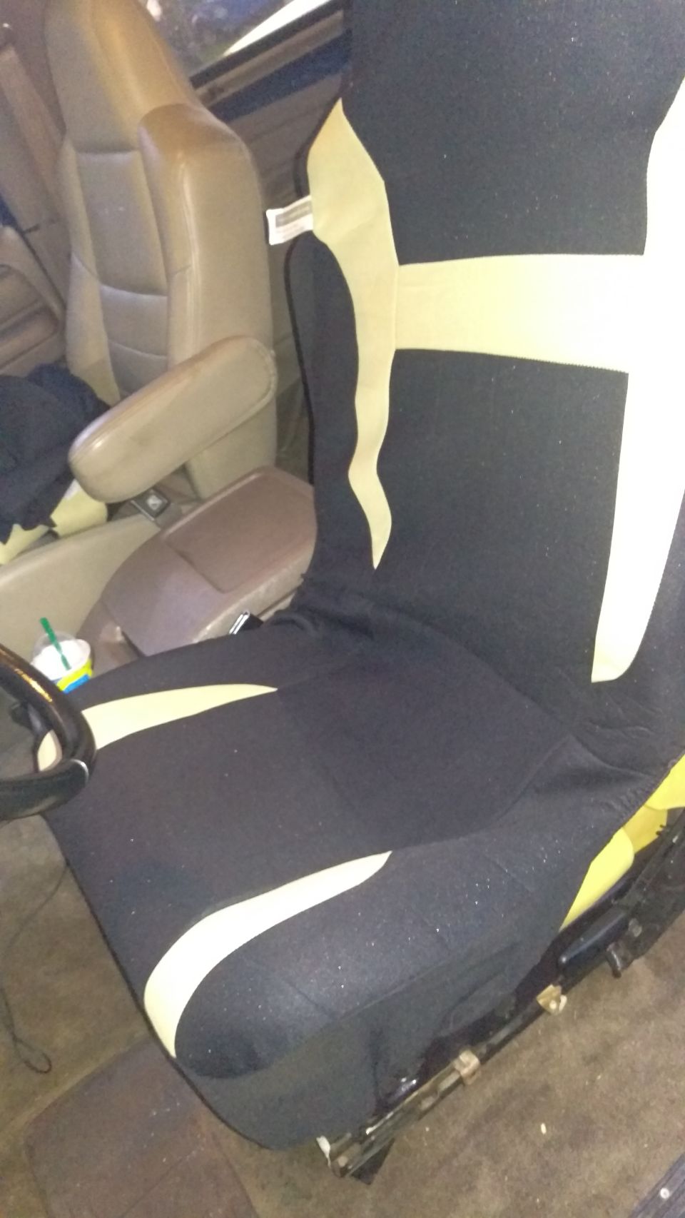 Black seat cover with tan accents over a tan vehicle seat. Steering wheel visible