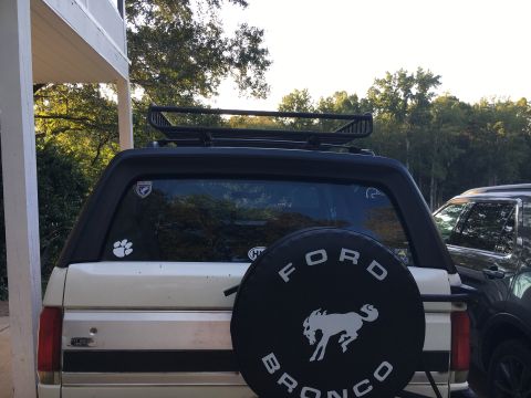 1988 Ford Bronco - This Ford Bronco features a spare tire cover with the Bronco logo and a roof rack, seen from the rear.