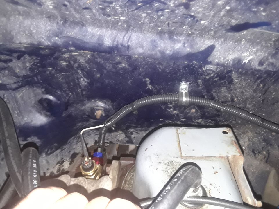 Close-up of engine bay wiring and a sensor. A hand is visible in the foreground