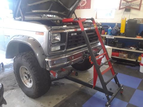1985 Ford Bronco - A silver 1985 Ford Bronco is shown from the front with its hood up, undergoing service.