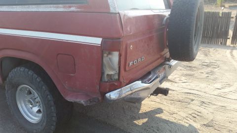 1981 Ford Bronco - Rear view of a red 1981 Ford Bronco showing collision damage to the taillight and bumper, with a spare tire mounted externally.