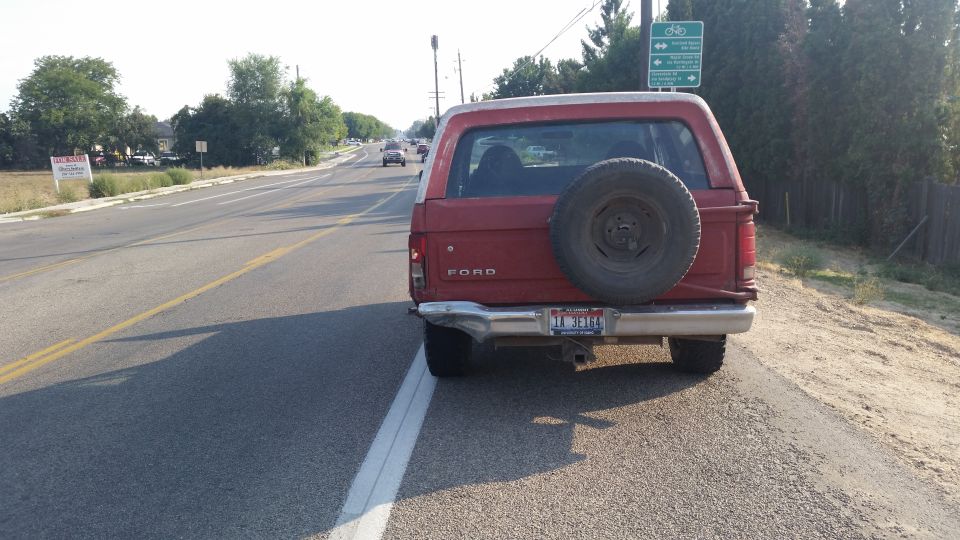Red Ford Bronco parked on the side of a road, spare tire mounted on the rear door