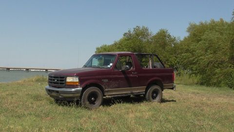 1996 Ford Bronco - This 1996 Ford Bronco is shown in a three-quarter front view, parked outdoors with a body of water and trees in the background.