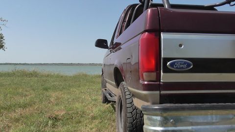 1996 Ford Bronco - A Ford Bronco is parked on a grassy area next to a body of water under a clear sky.