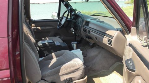 1996 Ford Bronco - The interior of a maroon SUV is shown, cloth seats and a tan dashboard with various controls and gauges.