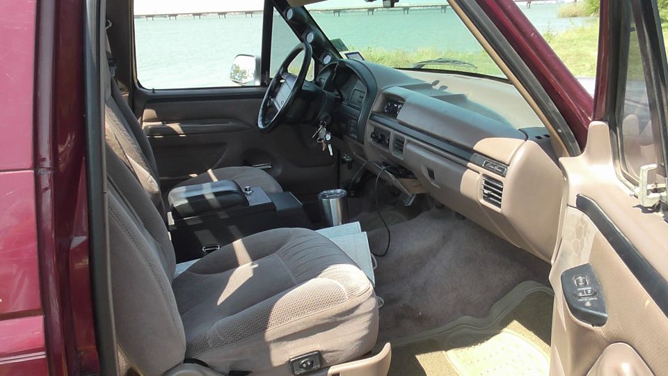 Interior of a maroon SUV, showing front seats, dashboard, and steering wheel. Water and a distant structure visible through the windows