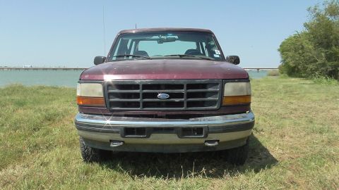 1996 Ford Bronco - Front view of a maroon 1996 Ford Bronco parked on a grassy area with a body of water and a bridge in the background.