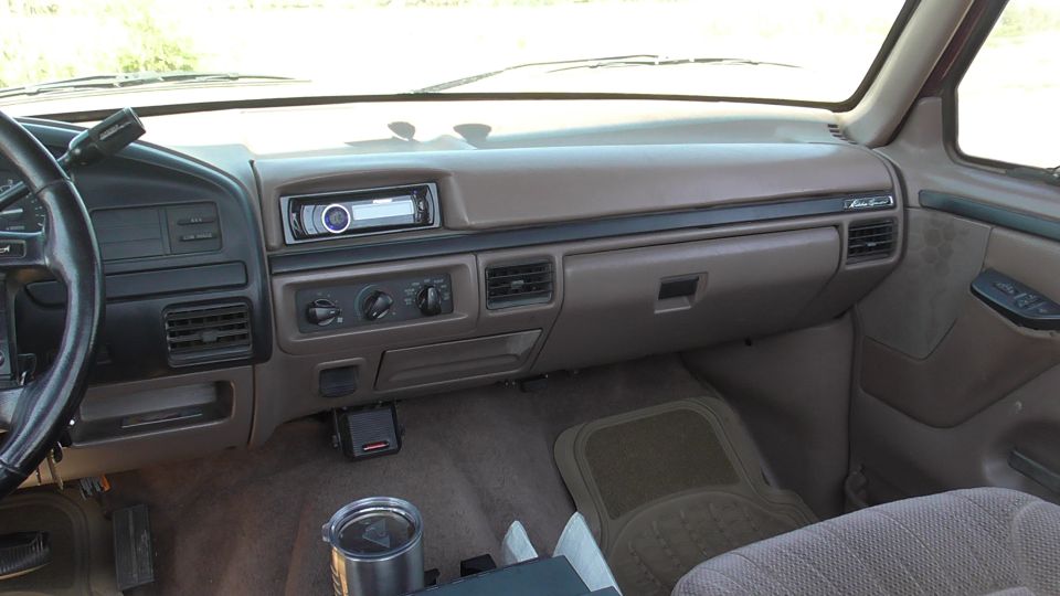 Brown dashboard with aftermarket stereo, climate controls, and steering wheel. Cup holder visible