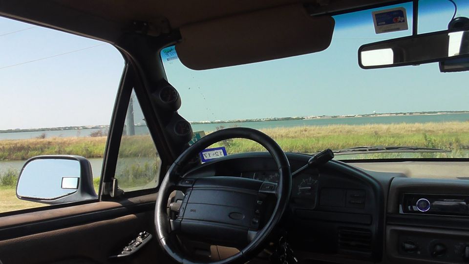 1996 Ford Bronco interior showing steering wheel, dashboard, and side mirror with a view of water outside