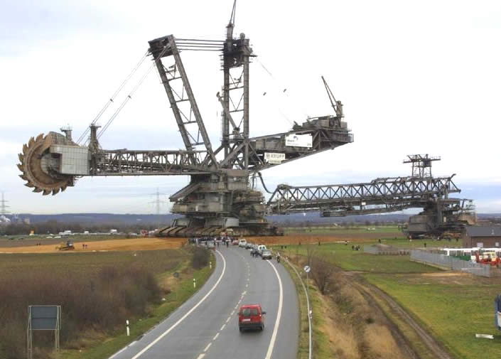 Giant bucket-wheel excavator with a road and a red car in the foreground