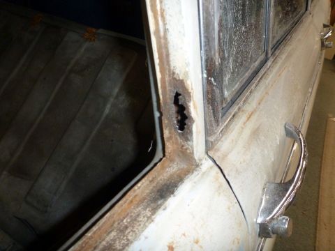 1962 MG B - Close-up of a rusty car door frame and interior paneling, with a chrome door handle visible.