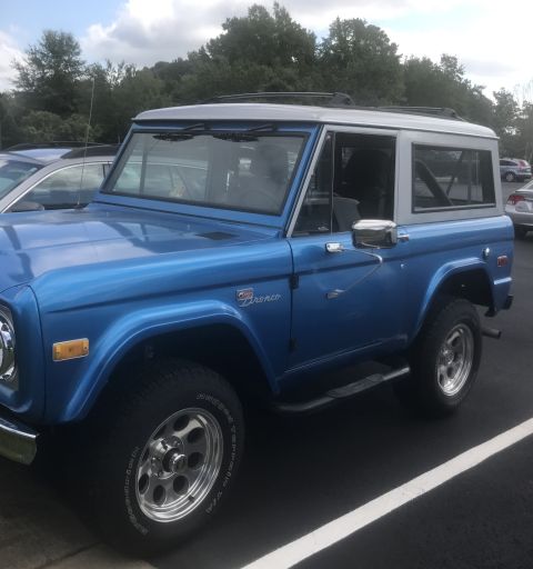 1974 Ford Bronco - This 1974 Ford Bronco is parked in a lot with trees and other vehicles in the background.
