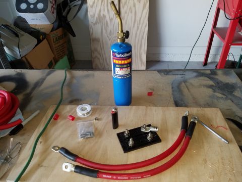 1994 Ford Bronco - Tools and parts for car battery maintenance, including a propane torch and heavy-duty red battery cables.