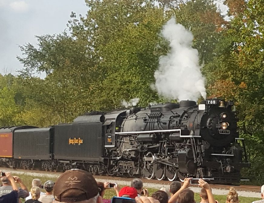 Steam locomotive with number 765, emitting smoke, viewed from the front-right