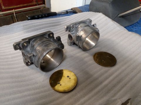 1995 Mercury Grand Marquis - Two throttle bodies, one appearing older and dirtier than the other, are laid out with brass plates on a padded surface.
