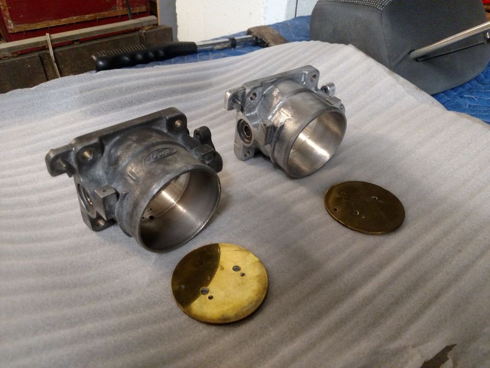 Two throttle bodies and brass plates on a padded surface