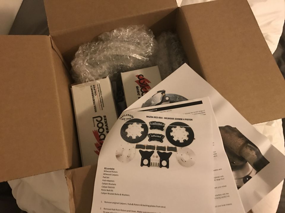 Box of car brake parts, including rotors, calipers, and instructions labeled for Mazda RX3-RX4