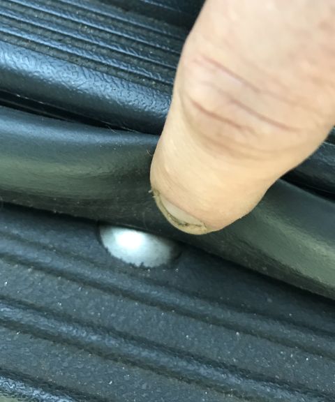 1995 Ford Bronco - A finger presses down on a black rubber seal, revealing a silver screw head on a textured surface.