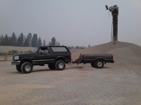 1995 Ford Bronco - A black Ford Bronco tows a trailer through a gravel pit, with a large pile of gravel and industrial equipment visible.