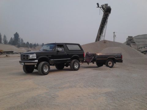 1995 Ford Bronco - A black Ford Bronco tows a trailer through a gravel pit with industrial equipment in the background.