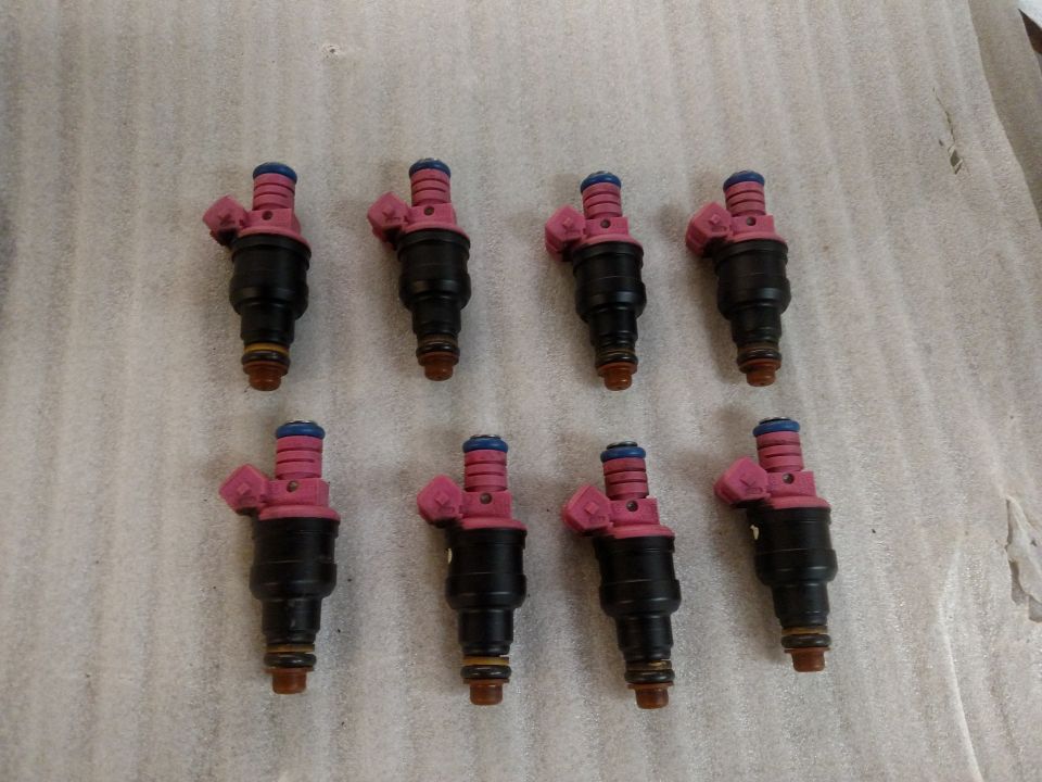 Eight black fuel injectors with pink tops and blue bands, laid out in two rows