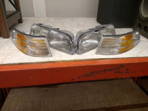 1995 Mercury Grand Marquis - Four automotive lights, including headlights and corner lights, are displayed on a shelf.
