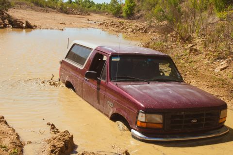 1996 Ford Bronco - A maroon 1996 Ford Bronco is partially submerged in thick mud and water.