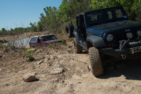 1996 Ford Bronco - A red SUV navigates a challenging off-road course, getting stuck in a shallow body of water.