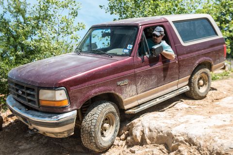 1996 Ford Bronco - A maroon 1996 Ford Bronco navigates a rocky off-road path with a driver inside.