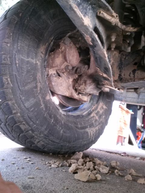 1996 Ford Bronco - The front wheel and suspension system of a vehicle are covered in mud and dirt, with debris on the ground.