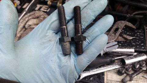 1981 Ford Bronco - A gloved hand displays two bolts, one appearing newer than the other, amidst a collection of automotive tools.