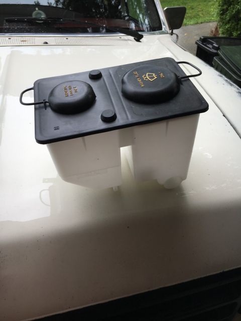 1988 Ford Bronco - A white vehicle's hood displays a black windshield washer fluid reservoir with two caps.